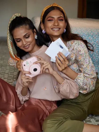 A joyful and interactive shot. The models smile as they hold up their instant camera and photos, creating a fun and engaging image that is perfect for a youthful fashion brand.