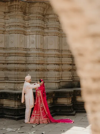 The groom gently lifts the bride's veil, a classic romantic moment set against the stunning architecture of a temple.