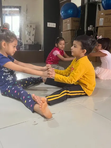 Young students work in pairs to help each other with seated stretches, fostering teamwork and friendship.