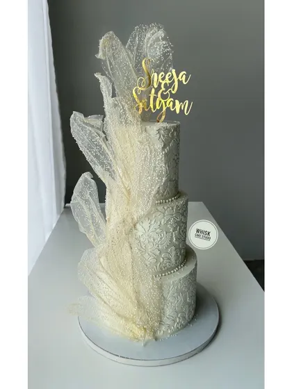 A three-tiered white beauty for a wedding. This cake features exquisite stencil work and shimmering wafer paper sails for a touch of modern elegance.