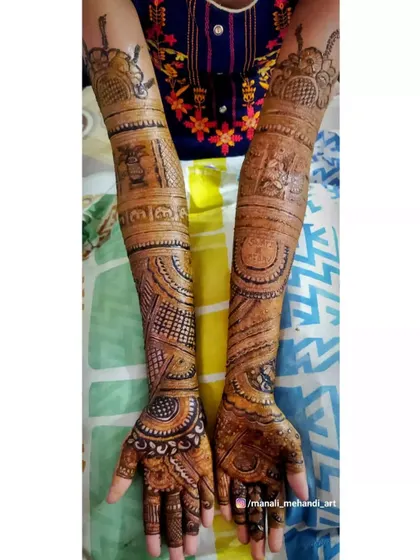 A complete view of a bridal mehandi with full arm coverage. The design includes traditional elements like a doli and kalash, along with the groom's name on the palm.
