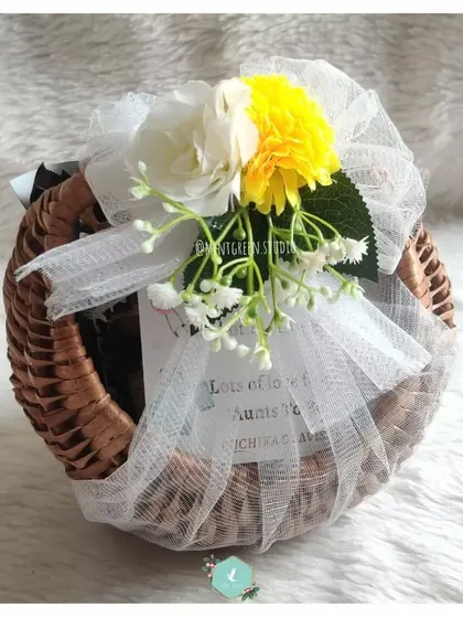 A mom-to-be hamper beautifully presented in a round cane basket. The white and yellow flowers on top add a fresh and cheerful touch.