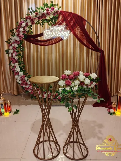 An elegant birthday setup using a circular frame decorated with artificial flowers and a draped cloth, offering a beautiful alternative to balloons.