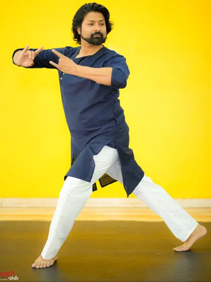 A portrait of me against a bright yellow background, demonstrating a classical dance pose.