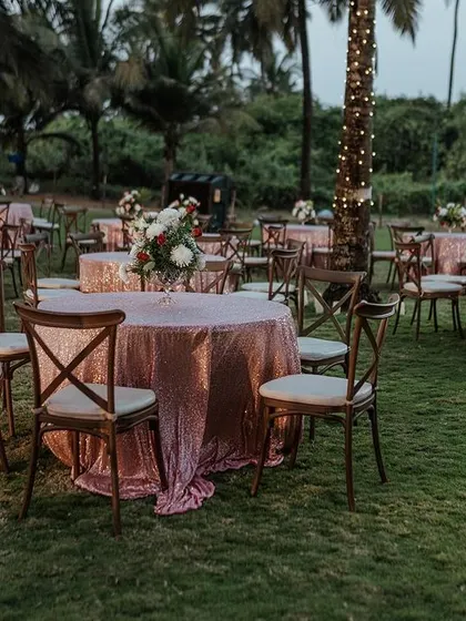 An elegant evening reception setup on a lush lawn by the beach. The sequined tablecloths and simple floral centerpieces add a touch of glamour to the outdoor setting.