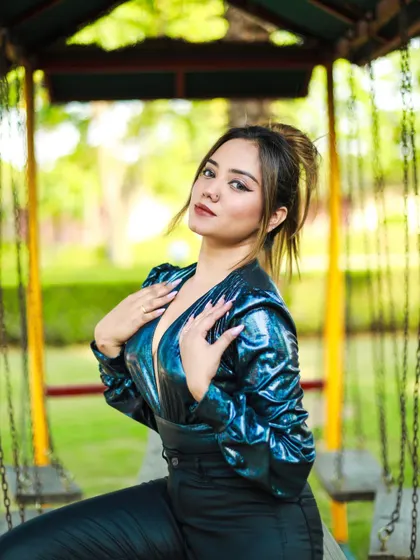 An outdoor shot in a park, featuring a model in a metallic blue bodysuit. The natural green background makes the shiny fabric stand out.