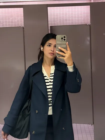 A college outfit dump starts with this mirror selfie in a classic trench coat and striped cardigan.