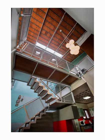 The Interlocking House features a fabricated light internal staircase with a woven steel mesh railing. This transparent structure allows light from the skylights above to filter down to the lower level, while beer bottle ends embedded in the wall create playful patterns of light.