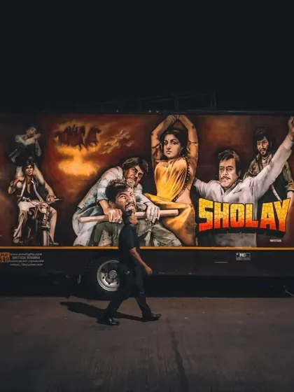 A classic, hand-painted mural of the iconic "Sholay" movie poster on the side of a truck. This is mobile street art, carrying a piece of Bollywood history through the lanes of Mumbai.