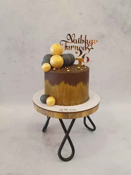 A decadent chocolate cake with a gold brushstroke effect. The chocolate drip and gold and grey spheres give it a modern and luxurious feel.