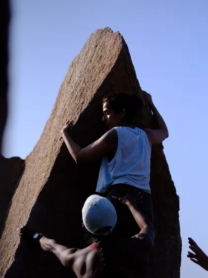 A climber ascends the iconic Left Arete on Rishimuk Plateau in Hampi. This shot captures the focus and strength required for such a beautiful and technical climb, with a spotter ensuring safety.