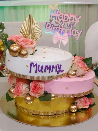 A stunning three-tier cake for a mother's birthday. The combination of white, pink, and gold tiers, adorned with fresh roses and gold spheres, creates a look of pure luxury and love.