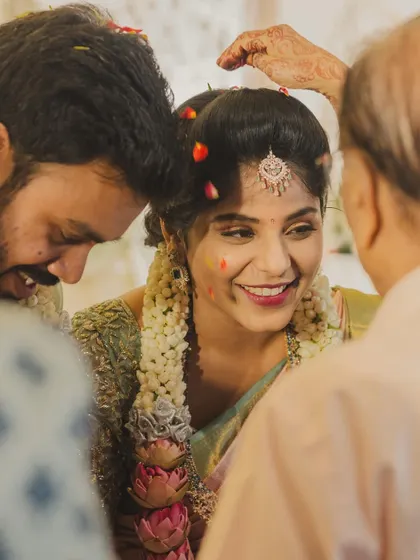 A joyful moment from a South Indian wedding, where the bride is blessed by her elders with flowers and rice.