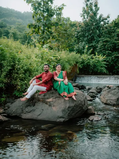 A peaceful pre-wedding portrait of a couple sitting on a rock by a stream.