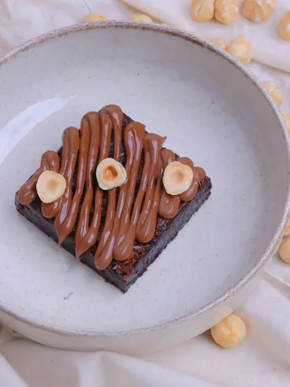 Our Hazelnut Brownie in a bowl, surrounded by whole hazelnuts. We use real nuts and a quality hazelnut spread to achieve its authentic flavour.