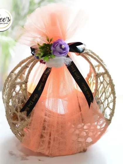 A close-up of the decorative wrapping on my exclusive Rakhi basket. The jute basket is wrapped in peach-colored tulle and tied with a black ribbon and a small floral bunch.