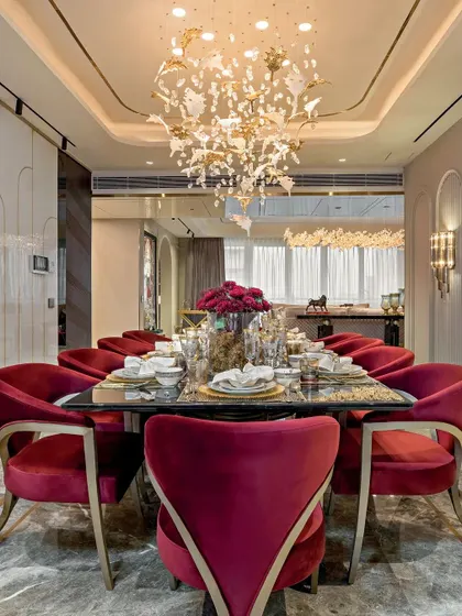 A dining room that makes a bold statement with its rich, red velvet chairs and a custom chandelier that resembles birds in flight. The dark marble table and gold accents create an atmosphere of pure opulence, perfect for formal entertaining.