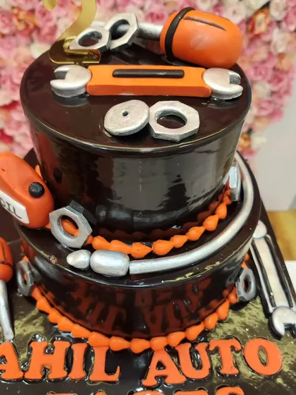 A clear, straight-on shot of the two-tiered automobile parts cake, highlighting the rich chocolate glaze and orange accents.