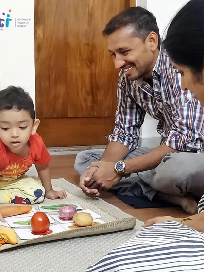 Parents smile as they watch their son confidently identify different vegetables using picture cards. This language activity is a simple yet effective way to build vocabulary.