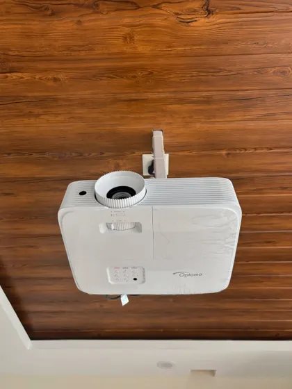 A close up of a ceiling mounted Optoma HD projector against a wooden ceiling. This shows how we can adapt the installation to different ceiling materials and styles for a secure and seamless fit.