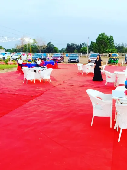 We cover large outdoor areas with carpeting to create a clean and defined party space. Here, a red carpet covers the lawn, with white garden chairs and tables set up for guests.