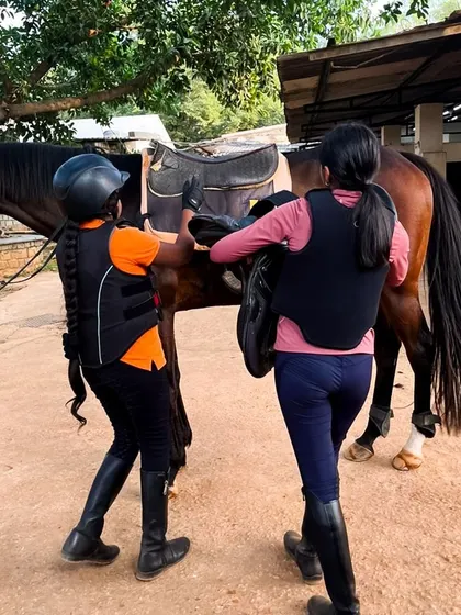 Two campers work together to properly place a saddle on their horse. Learning to tack up correctly is a fundamental skill that teaches responsibility and ensures the safety and comfort of both horse and rider.