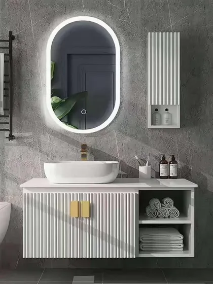 This bathroom design is clean and contemporary, with a white floating vanity featuring a fluted texture and gold hardware. The backlit oval mirror provides excellent task lighting while adding a soft, ambient glow to the room.