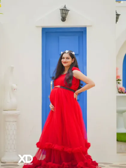 A graceful solo portrait of the mother-to-be in a vibrant red gown against a clean, modern backdrop.