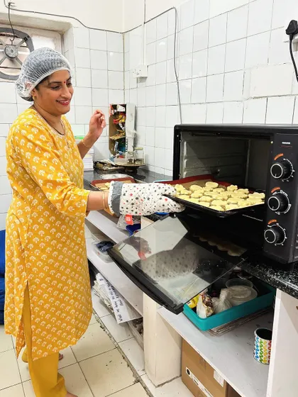 A smiling parent volunteer takes a fresh tray of cookies out of the oven. We are so grateful for our parents who bring their passions and skills into our school.
