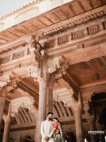 A low-angle shot looking up at a couple standing in a beautifully carved stone hall, emphasizing the intricate architecture of the Jaipur palace.