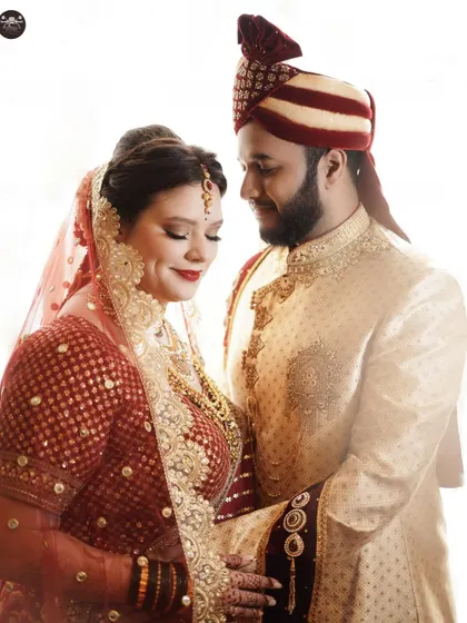 An intimate portrait of a bride and groom in their wedding attire. The high-key lighting creates a clean and bright look, emphasizing their features and the richness of their outfits.