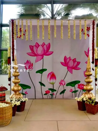 This photo booth setup for a half saree function features a hand-painted lotus backdrop. We framed the setup with jasmine garlands and placed traditional brass and wicker props in the foreground.