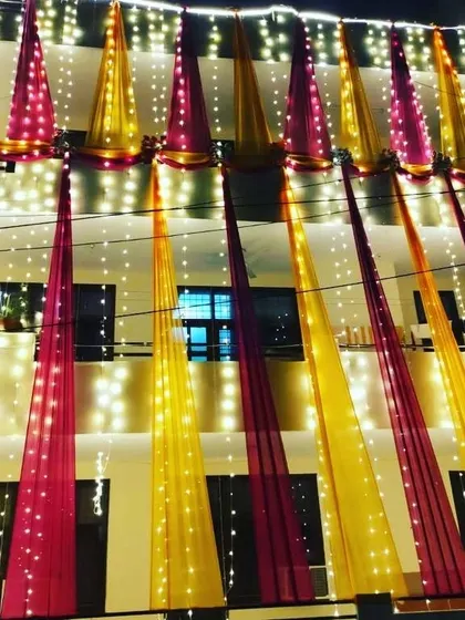 A multi-story house facade decorated with vertical drapes in pink and yellow, with each drape embedded with fairy lights for a stunning night view.
