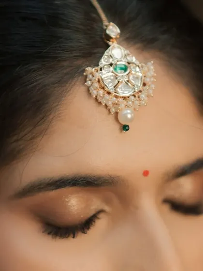 An extreme close-up on the eye makeup, showing the soft gold shimmer on the lids and the perfectly placed maang tikka.