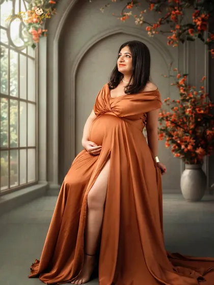 A beautiful portrait of a mom-to-be in a stunning bronze gown, seated in a studio setup designed to look like a sunlit room.