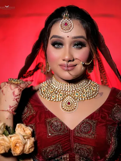 A classic bridal portrait against a bold red background. The bride's direct gaze and the impeccable details of her jewellery and makeup are the focus of this powerful shot.