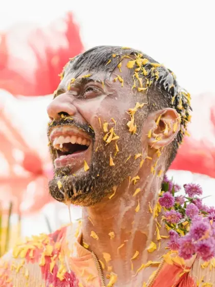 The groom's face is a picture of pure joy and laughter during his haldi. The colorful floral background adds to the whimsical and happy vibe of the celebration.