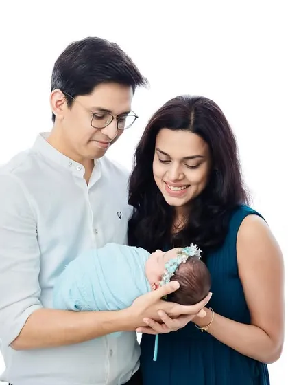 A classic family-of-three portrait against a clean white background. The focus remains entirely on the family and their new baby.