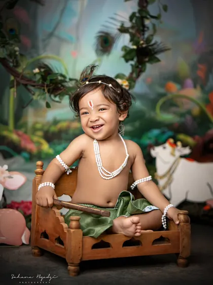 This little Krishna is all smiles, sitting on a tiny wooden bed in our enchanted forest. The setup is designed to be fun and engaging for children, resulting in natural, happy photos.