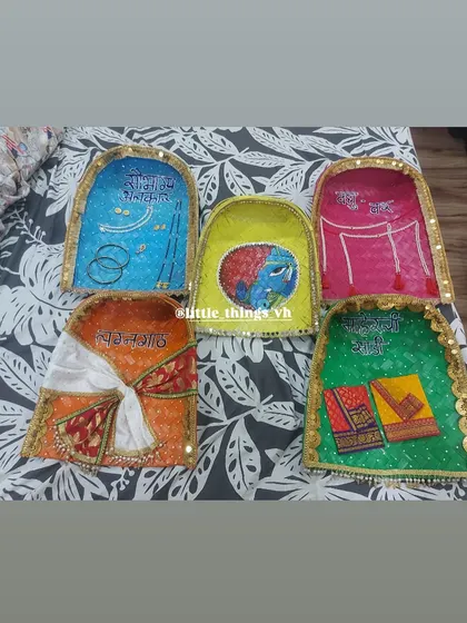 Hand-painted and decorated 'sup' or winnowing fans, each with a unique design like 'Maherchi Sadi' or 'Saubhagya Alankar'. These are beautiful, traditional additions to our wedding rukhwat.