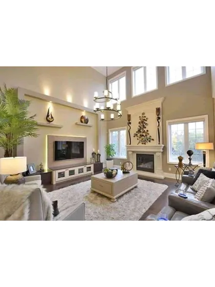 A living room with high ceilings and a traditional fireplace, creating a grand yet cozy feel. The large windows and statement chandelier enhance the room's spaciousness and elegance.