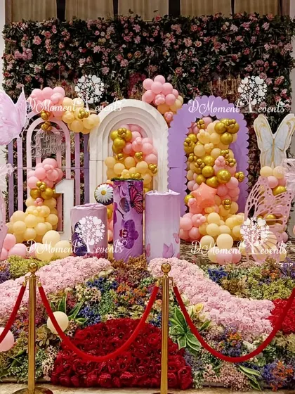 An incredibly detailed butterfly-themed stage featuring a lush floral base, multiple balloon arrangements, and delicate butterfly cutouts, all roped off for a grand reveal.