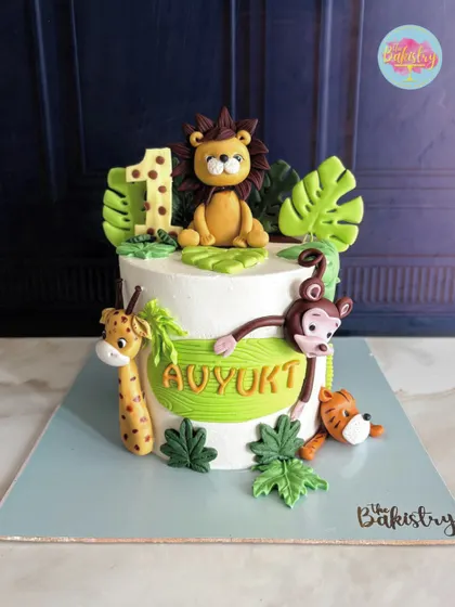 A full view of the handcrafted jungle cake for Avyukt's first birthday, with a lion, giraffe, monkey, and tiger.