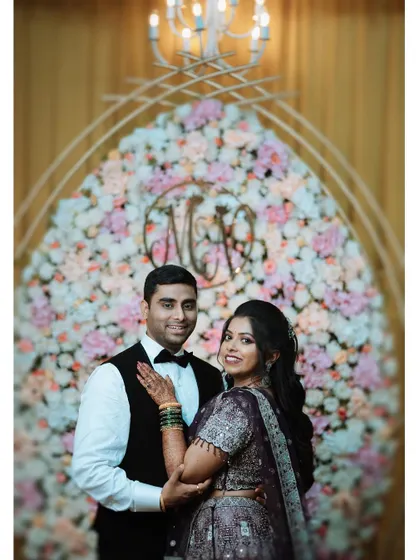A classic reception portrait of the couple in front of a floral arch with their monogram, looking happy and elegant.