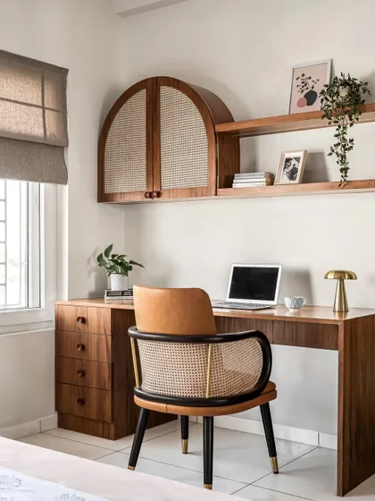 A modern and luxurious home office space with a wooden desk, a comfortable woven chair, and arched wall-mounted cabinets for storage.