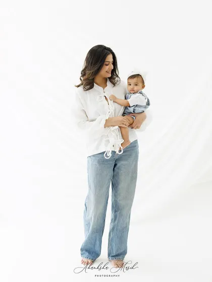 A beautiful, standing portrait of a mother holding her baby. The simple styling with a white shirt and jeans creates a classic, timeless look.