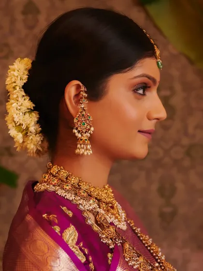 A profile view showcasing the intricate details of the bridal bun, adorned with fresh jasmine, and the elegant lines of her jewellery.