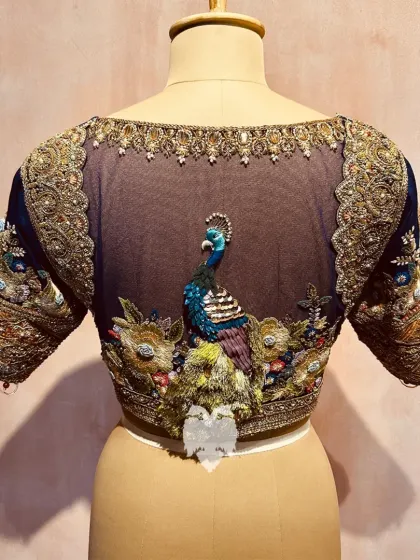 Inspired by the Katha Collection, this royal blue silk blouse features a sheer net back with an appliqué peacock, crafted with zardosi, stones, and pearls.