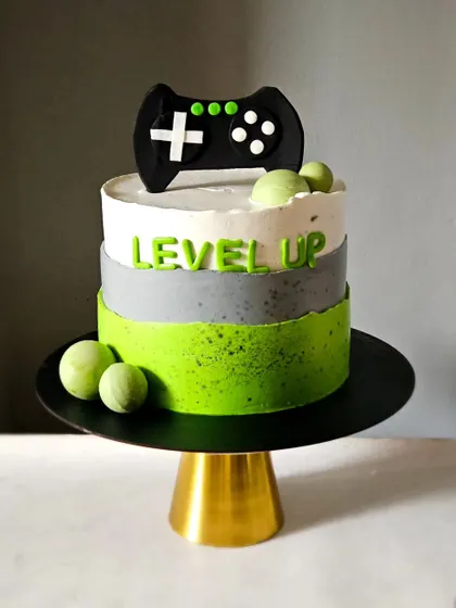 A modern and minimalist gaming-themed cake. The design features a "Level Up" message and a clean, three-toned color scheme in green, grey, and white, topped with a fondant game controller.