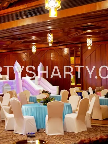 A wide view of the party space, showing mermaid-themed table settings with blue tablecloths and a large inflatable bouncy slide in the background for entertainment.